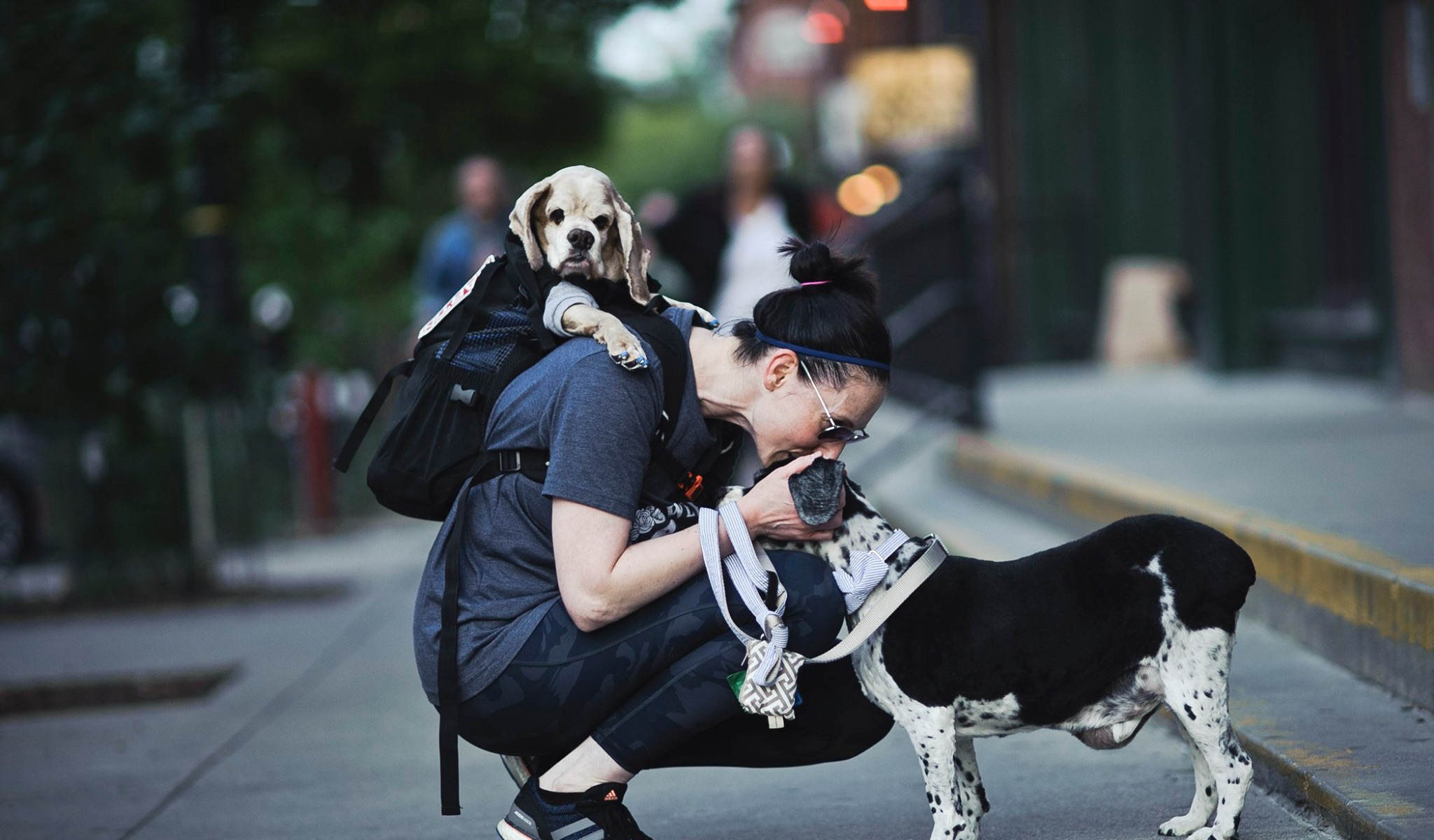 A woman shows affection toward her two dogs on a city street